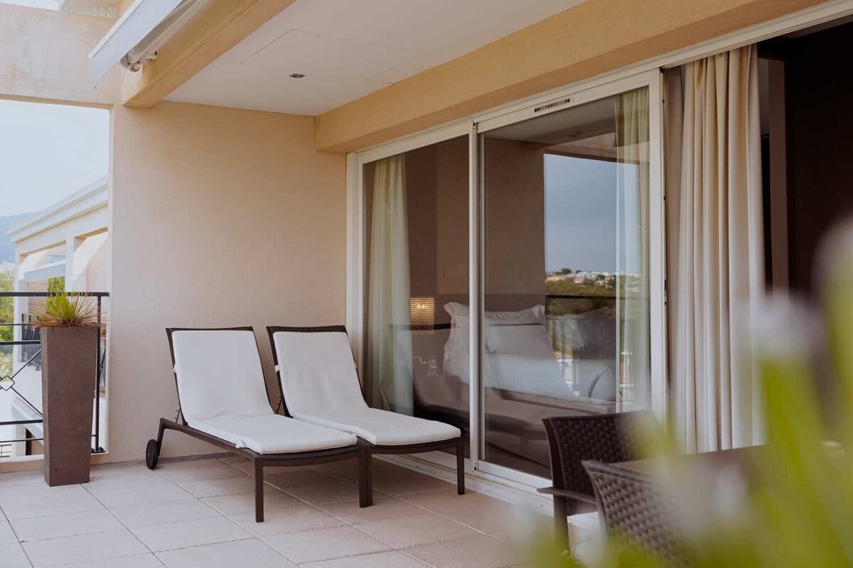 Two lounge chairs sit on a balcony next to a sliding glass door