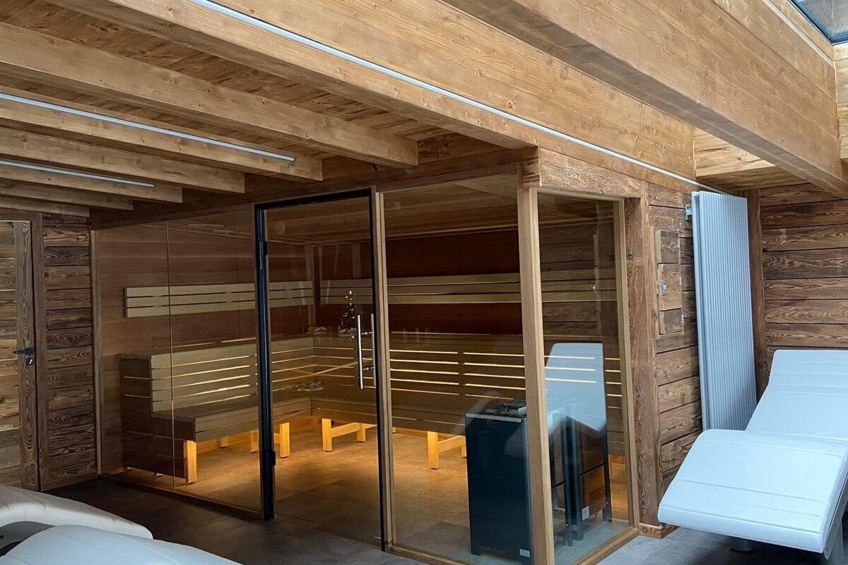 A wooden sauna with a glass door and chairs