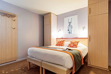 Modern bedroom featuring a double bed with orange pillows, flanked by light wood wardrobes and a deer painting on the wall.