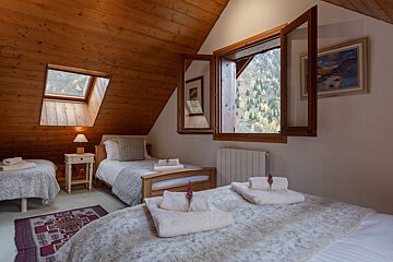 Cozy attic bedroom with three beds, a wooden ceiling, and stunning mountain views through open windows and a skylight.