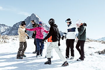 A group of people standing in the snow with a mountain in the background