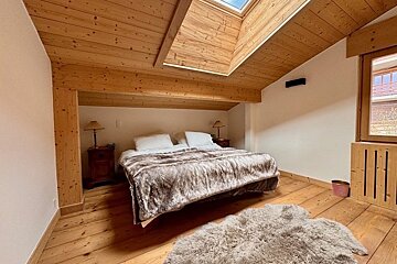 Cosy attic bedroom with natural wood finishes, a skylight, a plush fur blanket on the bed, and a fluffy matching rug on the floor.