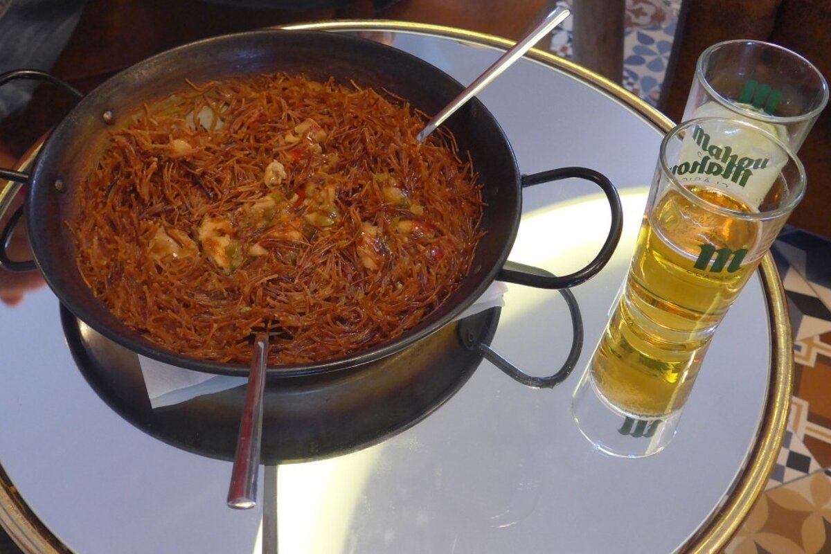 a wok with noodles and a glass of beer
