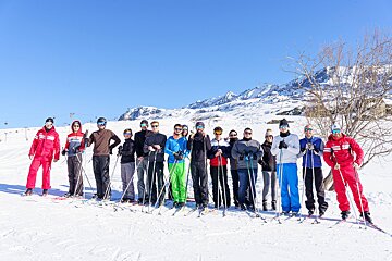 A group of skiers are posing for a picture and one of them is wearing a jacket that says asics