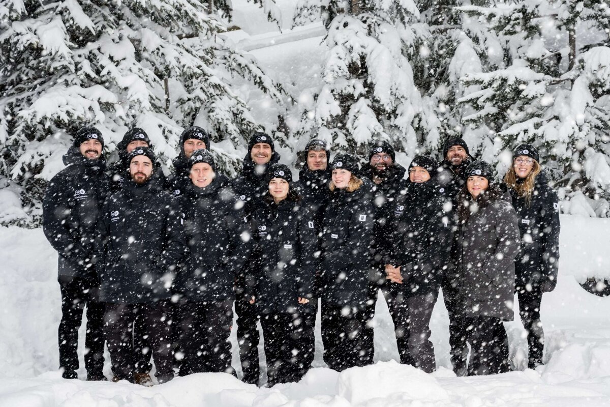 A group of people standing in the snow wearing black jackets and hats with the letter o on them