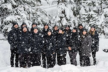 A group of people standing in the snow wearing black jackets and hats with the letter o on them