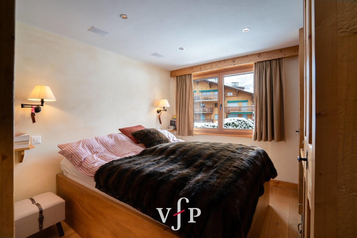 Cozy bedroom with a wooden bed, furry blanket, and a window revealing snowy chalets.