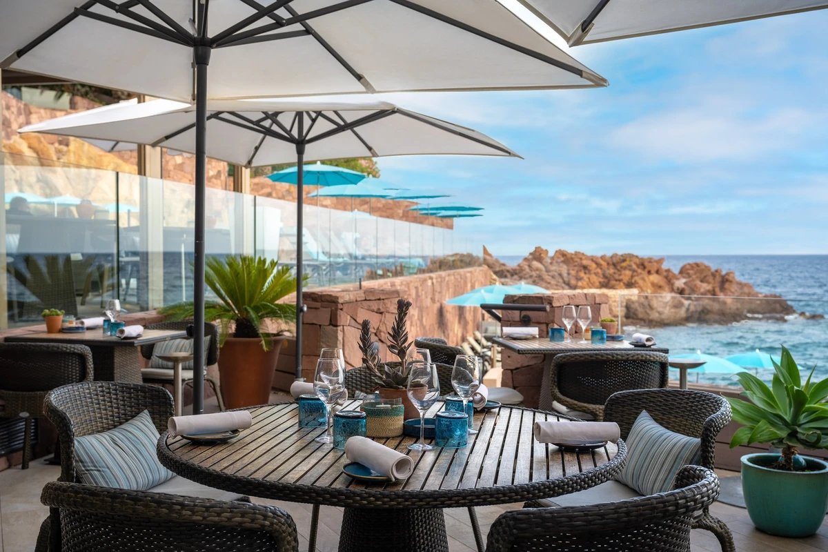 A patio with tables and chairs and umbrellas overlooking the ocean