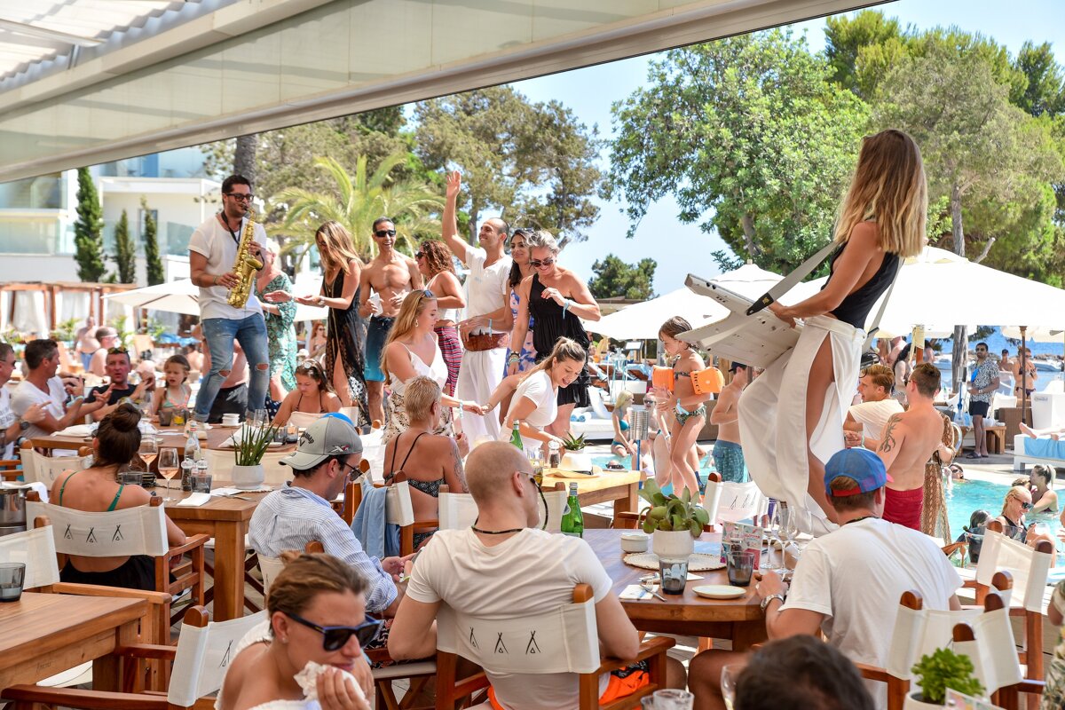 A man playing a saxophone is surrounded by people at a restaurant called l & a