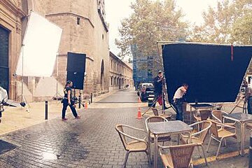 A group of people are standing on a brick sidewalk next to tables and chairs