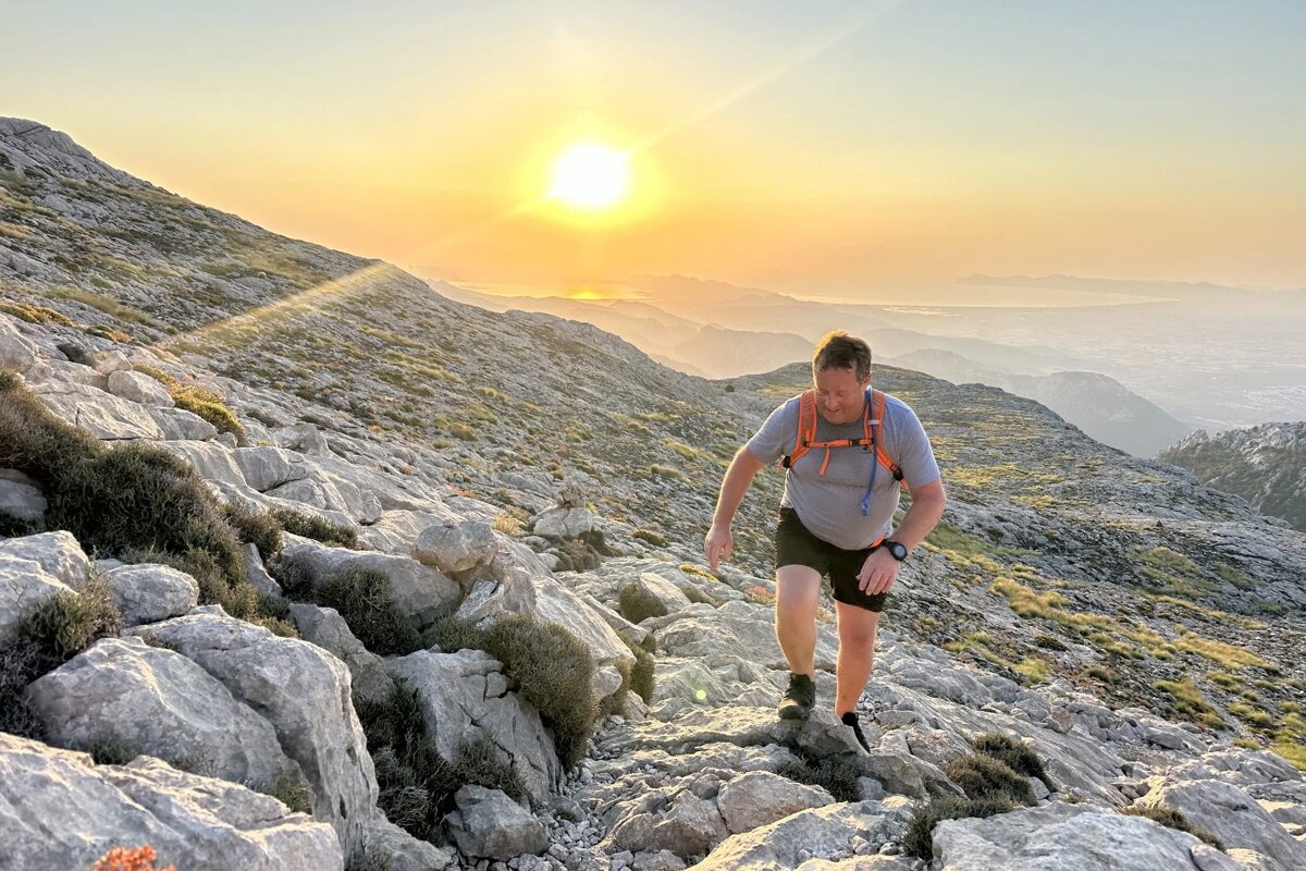 A man hiking up a rocky mountain at sunset