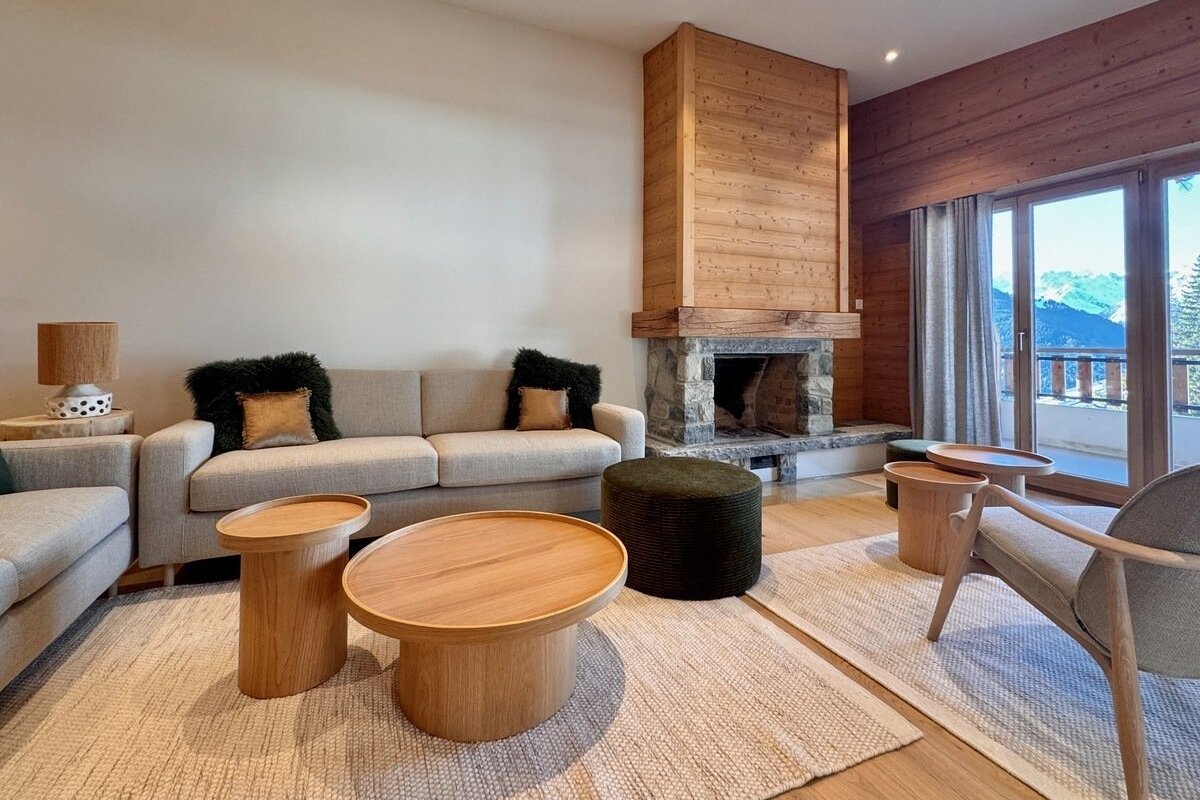 Cozy living room with fireplace, comfy sofas, wooden coffee tables, and a stunning mountain view from the balcony.