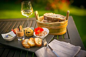 A wooden bucket filled with bread sits on a table next to a glass of wine