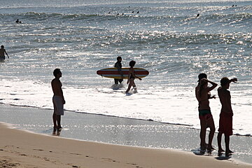 surfers in water and standing on the beach