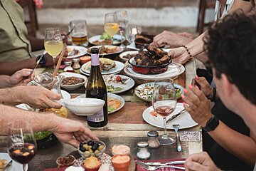 A group of people are sitting at a table with plates of food and a bottle of wine