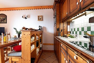 Rustic kitchen with warm wooden cabinetry, a green and white checkered tile backsplash, and an adjacent dining table.
