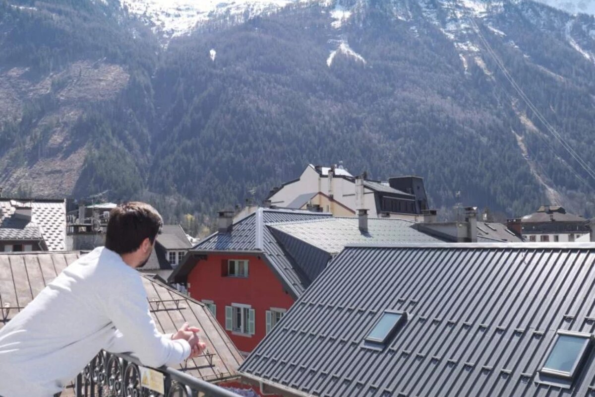 A man stands on a balcony overlooking a mountain range