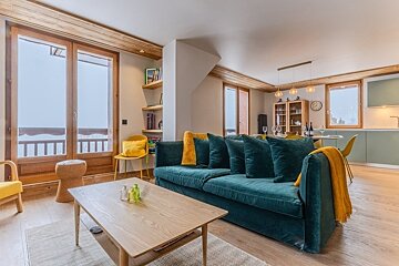 Modern living room featuring a teal velvet sofa with yellow accents, a wooden coffee table, and large glass doors leading to a balcony.