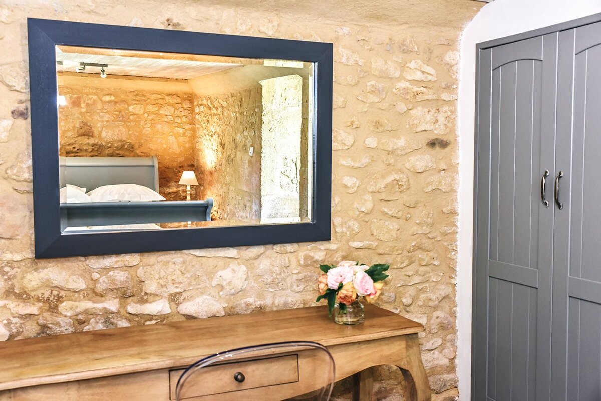 A large mirror hangs above a desk in a bedroom