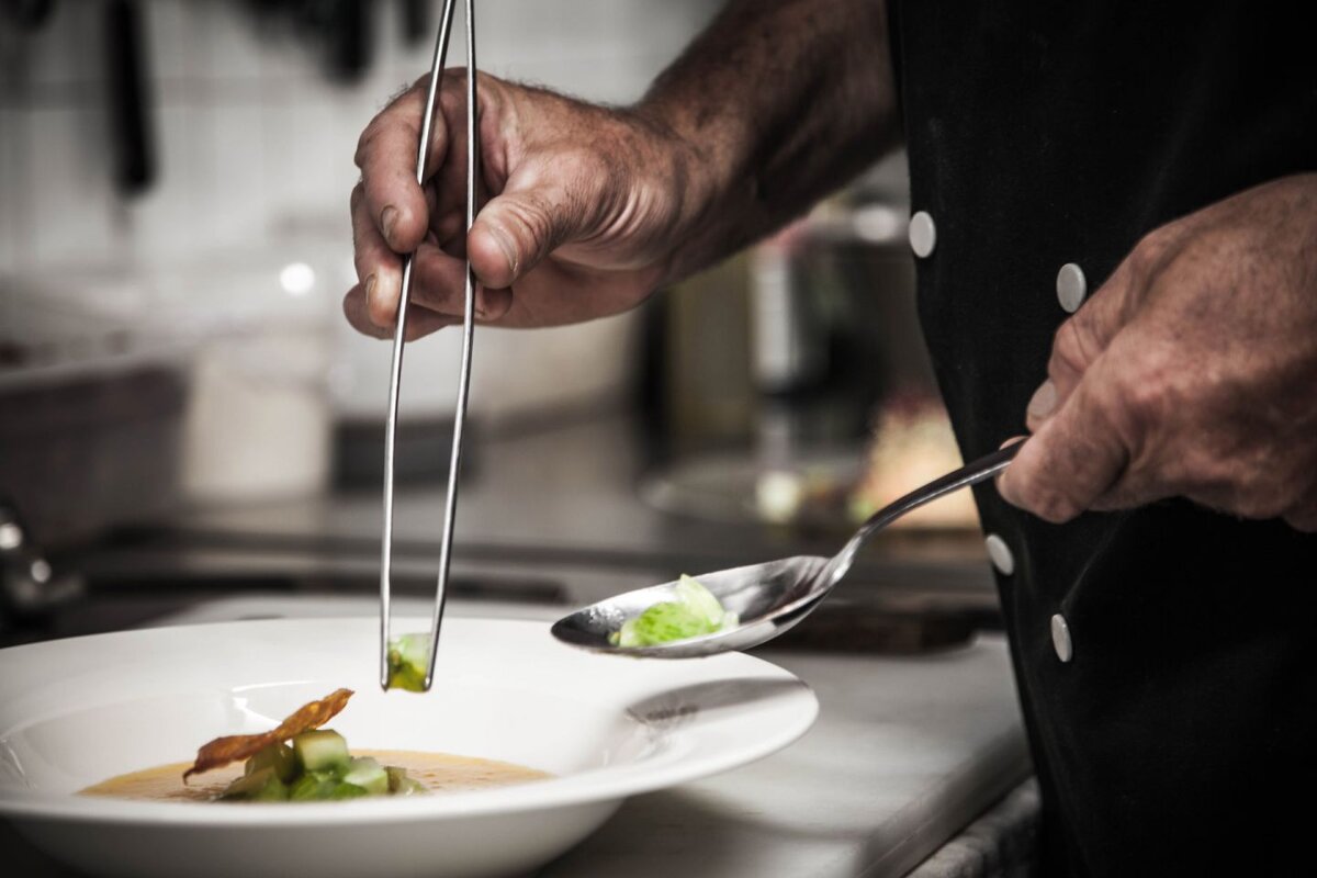 A chef prepares a plate of food with tongs and a spoon