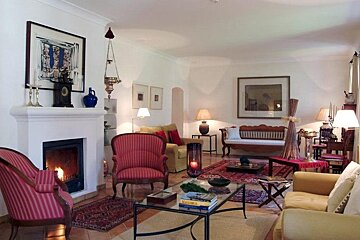 A cozy, traditional living room features a lit fireplace, red and yellow seating, ornate rugs, and classic decor, creating a warm ambiance.