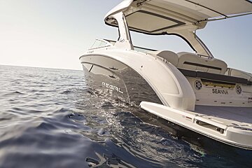 A sleek white and grey Regal Seanna boat cruises on calm, sparkling blue water under a bright sky, with sunlight reflecting off its hull.