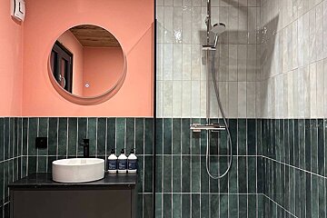 A bathroom with green and white tiles and a round mirror