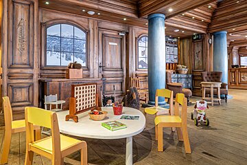 Cozy, wood-paneled kids' play area with yellow chairs, games, and toys. Faux windows show snowy mountains, while blue columns add charm.