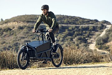 A man is riding a cargo bike on a dirt road