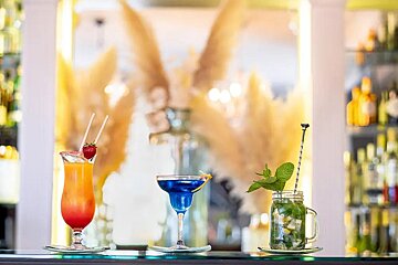 Three different cocktails are on a bar including a blue martini