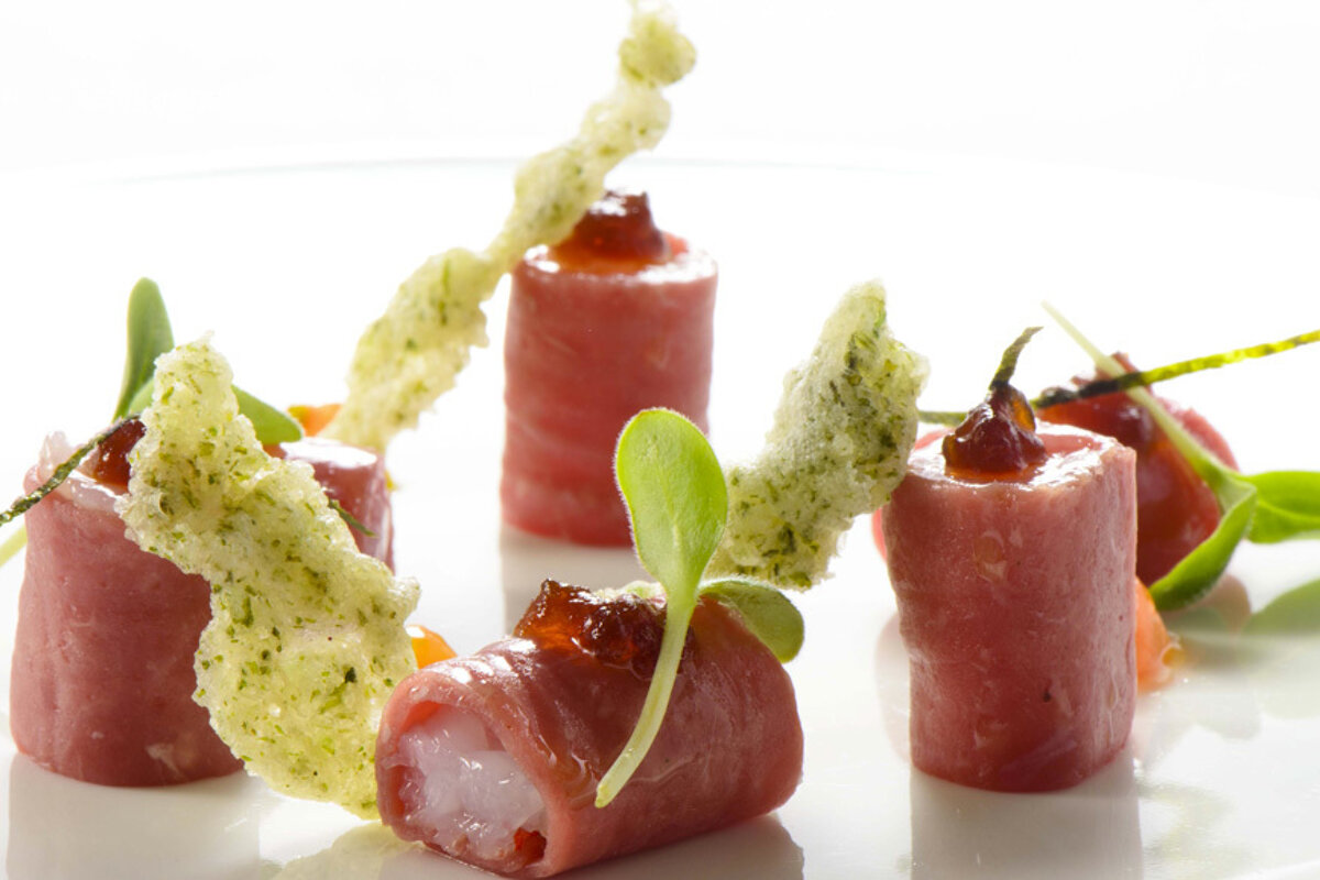 A white plate topped with a few rolls of meat and vegetables