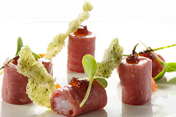A white plate topped with a few rolls of meat and vegetables