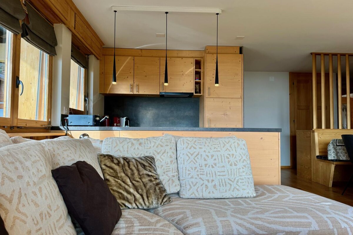 A living room with a couch and pillows and a kitchen in the background