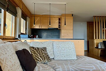 A living room with a couch and pillows and a kitchen in the background