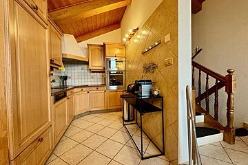 A kitchen with wooden cabinets and a staircase in the background