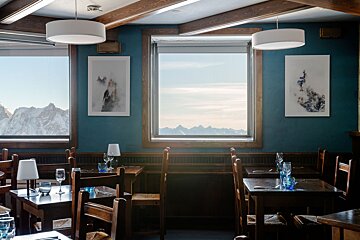 A restaurant with tables and chairs and a large window with mountains in the background