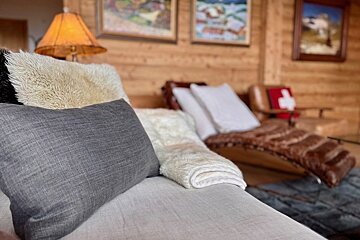 Cozy cabin living room featuring a grey pillow and fuzzy throw blanket on a sofa, with a leather chaise lounge in the background.