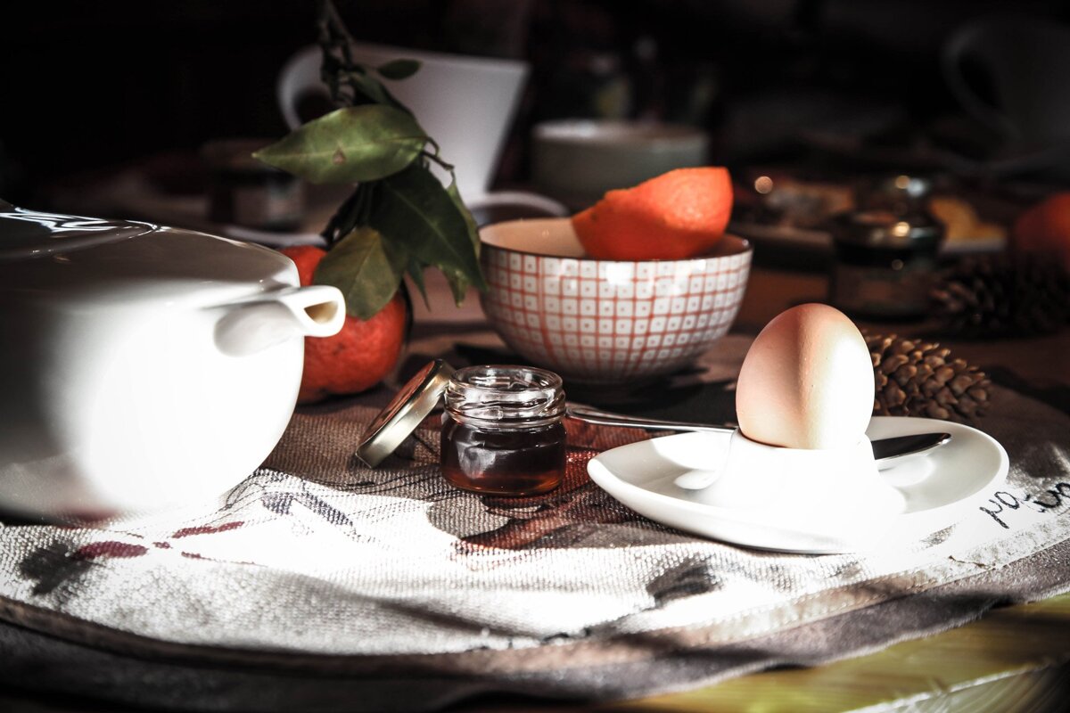 A jar of honey sits on a table next to an egg