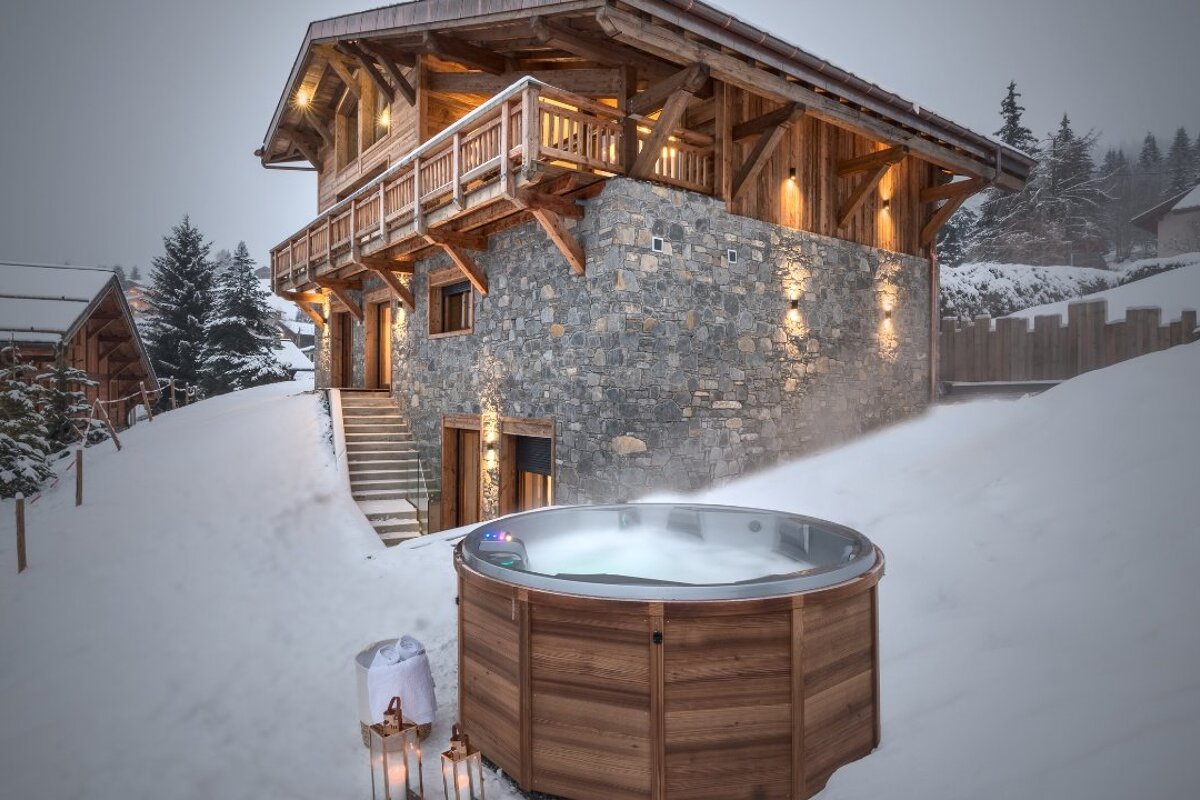 A wooden hot tub sits in front of a stone building
