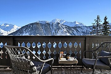A balcony with two chairs and a tray of food with mountains in the background