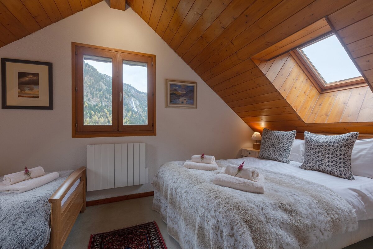 Cozy attic bedroom featuring wood ceilings, a double bed, single bed, and a window with a stunning mountain and waterfall view.