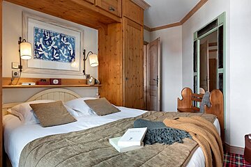 Cozy rustic bedroom with wooden cabinetry, a made bed with books and knitted throws, and a framed blue bird print on the wall.