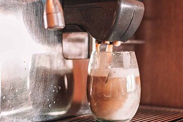 A coffee machine dispenses a layered latte into a clear glass, with reflections visible.