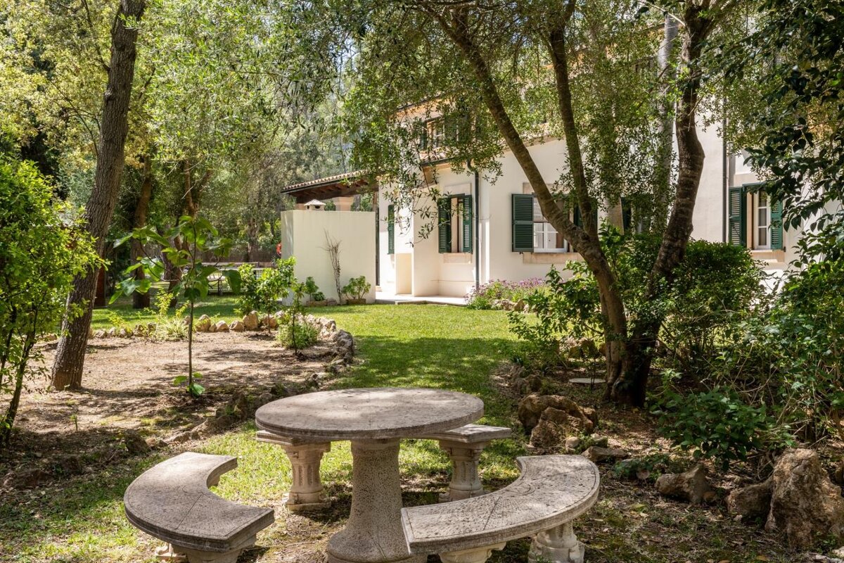 A stone picnic table sits in front of a house with green shutters