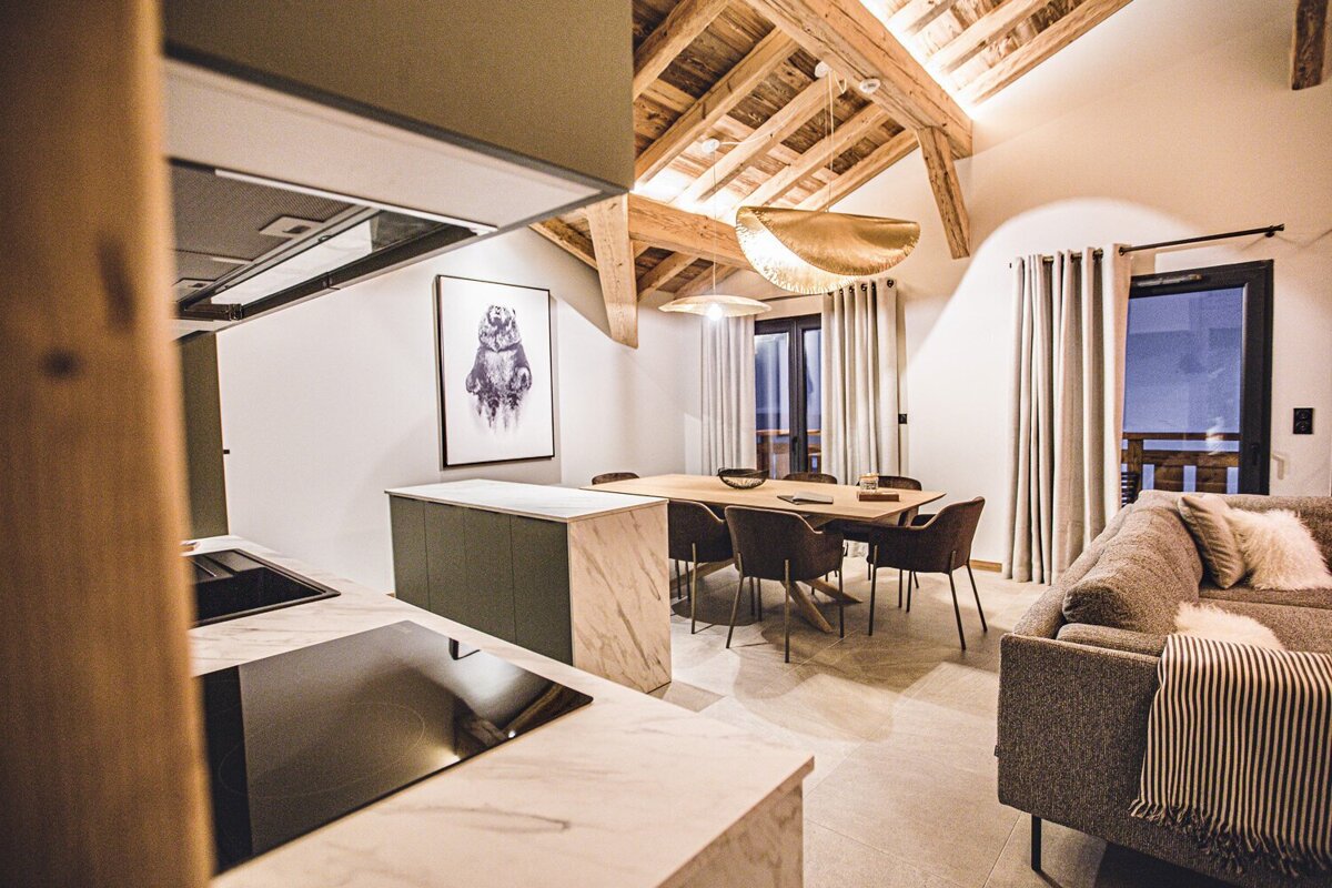 Stylish open-plan kitchen, dining, and living area with exposed wooden beams, chic lighting, a large bear art print, and balconies.