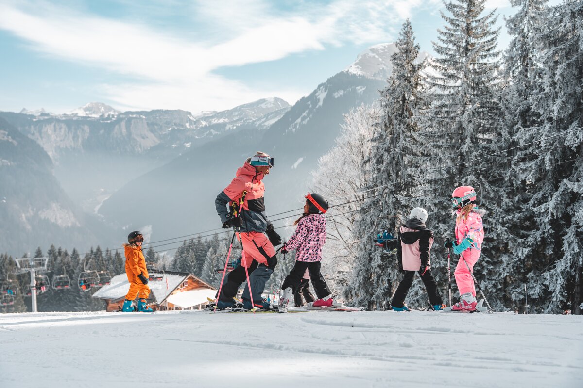 A group of people skiing down a snowy slope with mountains in the background