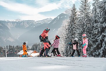 A group of people skiing down a snowy slope with mountains in the background