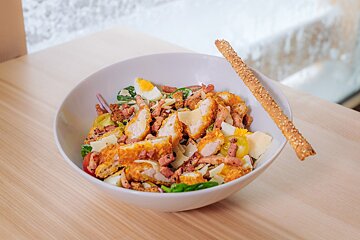 A salad in a white bowl with a bread stick in it