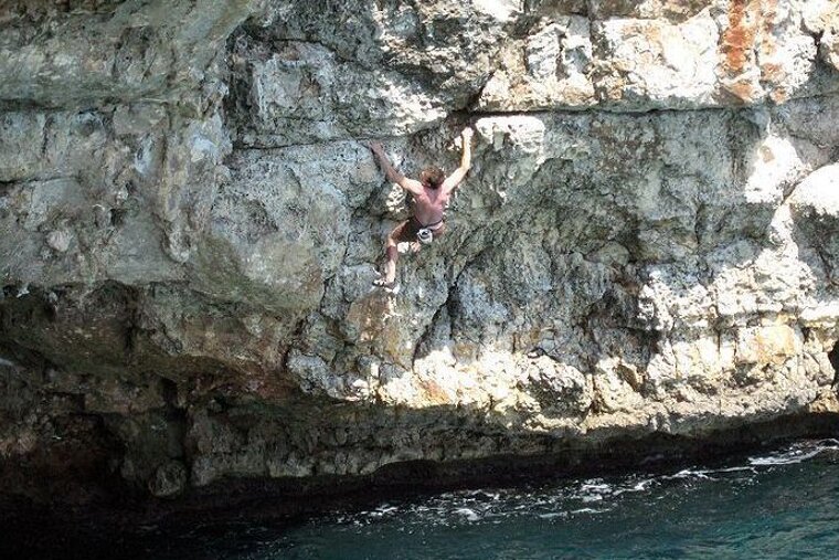 A man is climbing a cliff overlooking the ocean