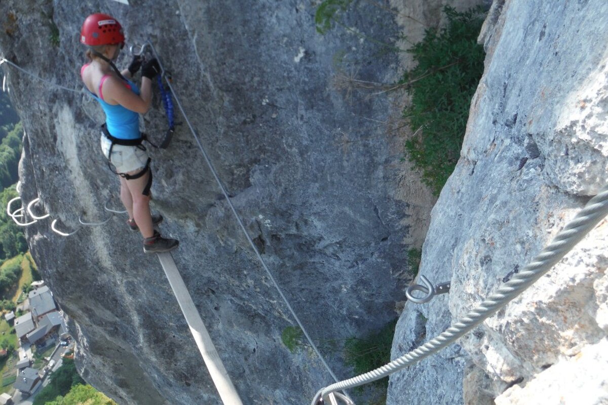 a woman standing on a wooden plank half way up a rock face